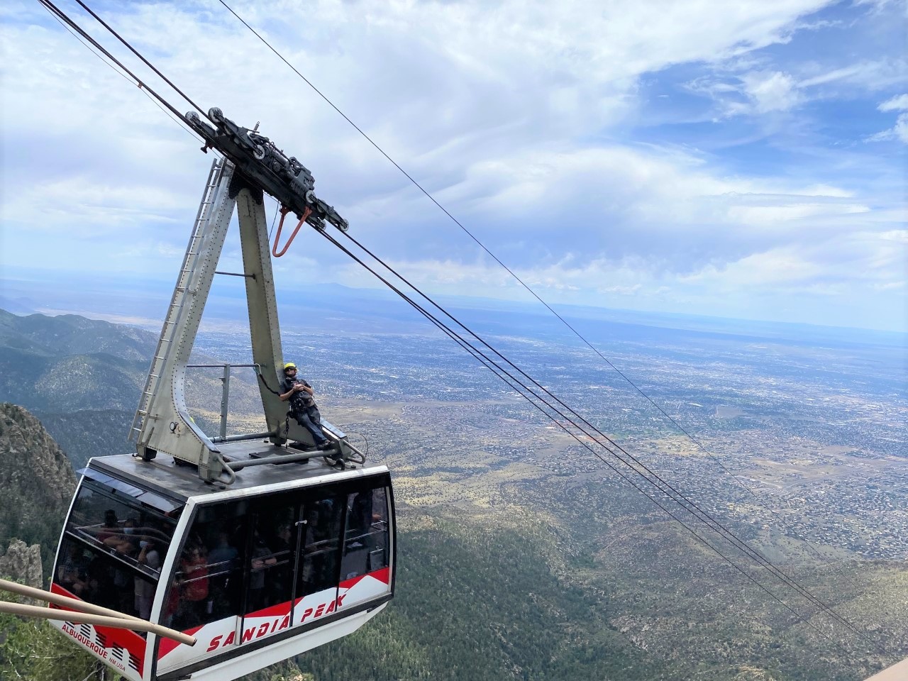 The Sandia Peak Tramcar, the cables, the view of Albuquerque, & a worker riding on top of the tramcar.